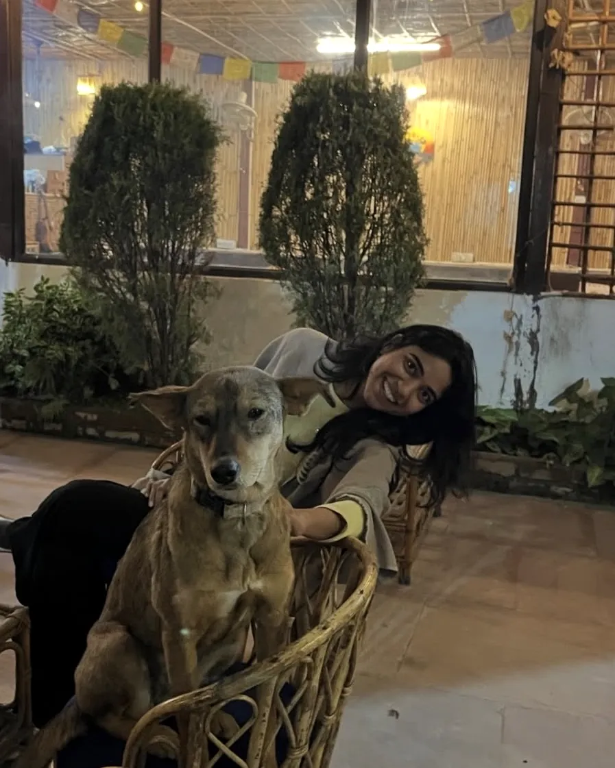 Abha seated in a wicker chair with a dog, in Rishikesh